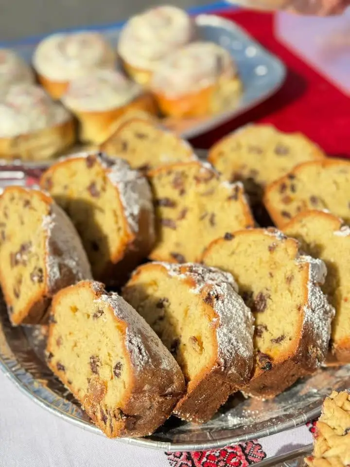 Sliced raisin sweet bread with cinnamon rolls behind on a silver platter