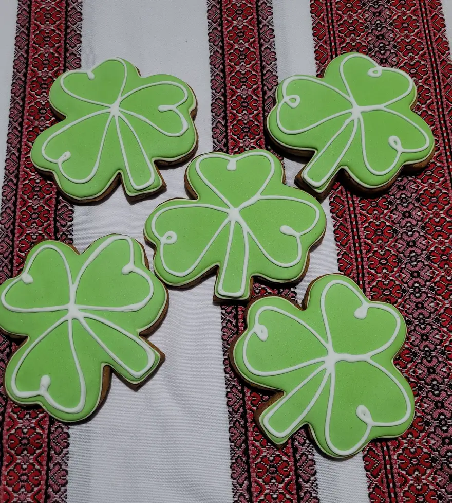Green shamrock iced cookies resting on a red and white Ukrainian embroidered cloth